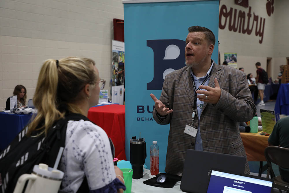 A representative from Burrell Behavioral Health speaks with a C of O student about future employment opportunities. 